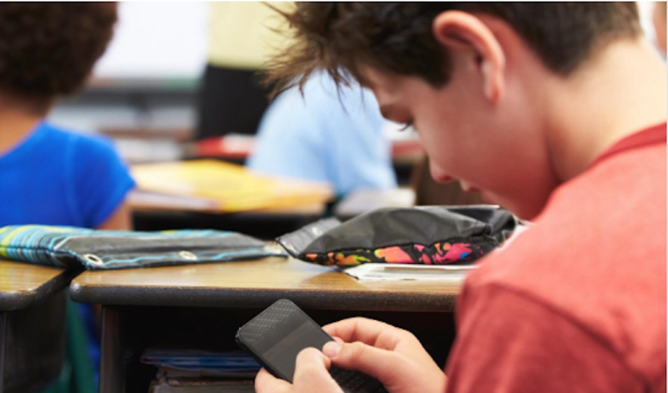 boy at desk sneaking cell phone use during class