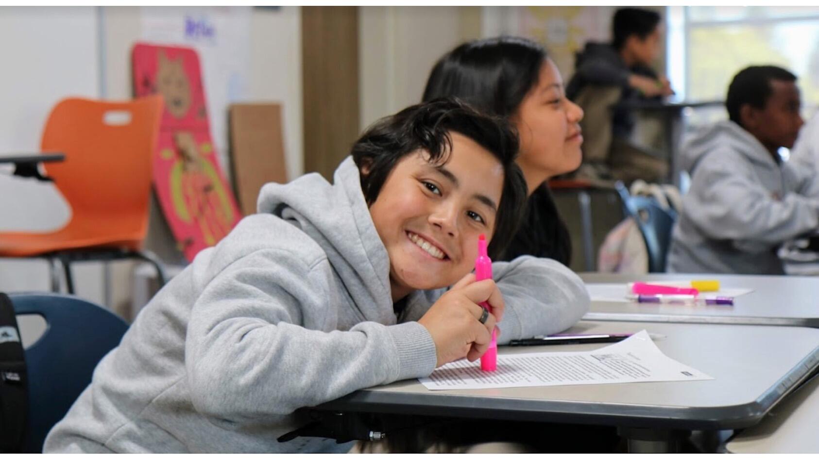 middle school boy smiling and leaning over desk