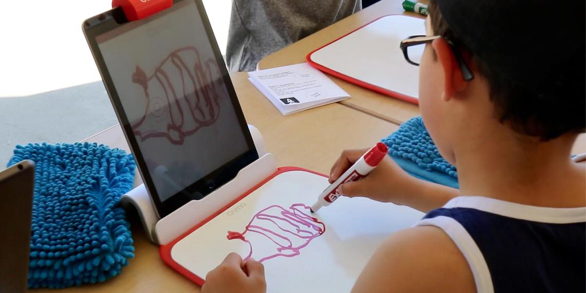 young boy drawing on paper as screen captures his art digitally