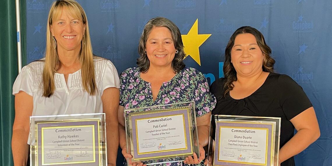 three smiling women holding framed award certificates.