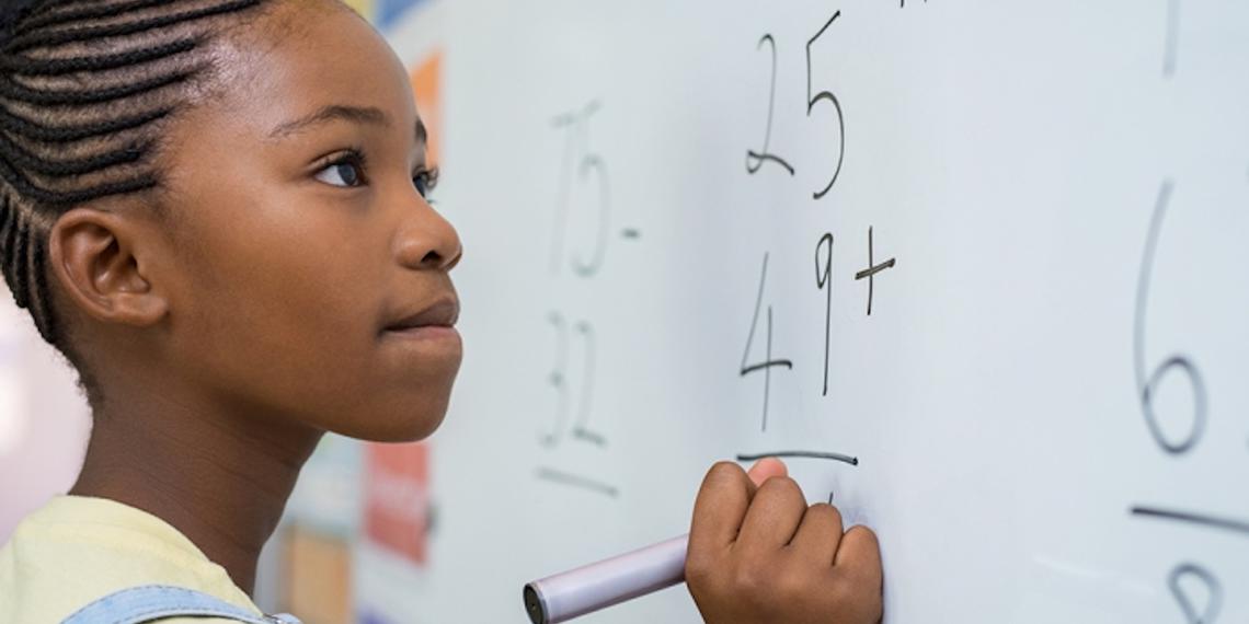 young girl working a math problem on a white board