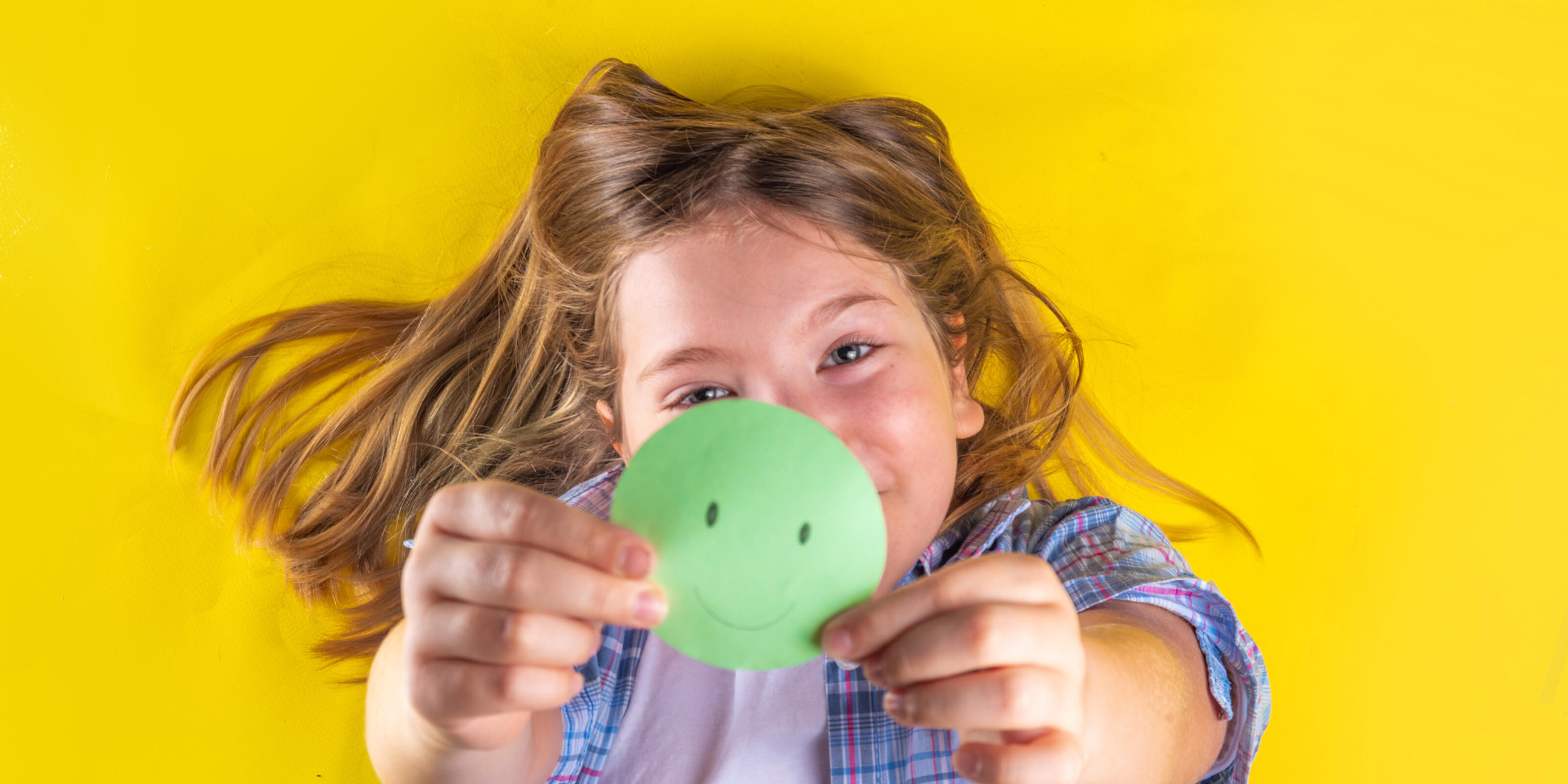 smiling young girl holding a green circle with a happy face drawn on it.